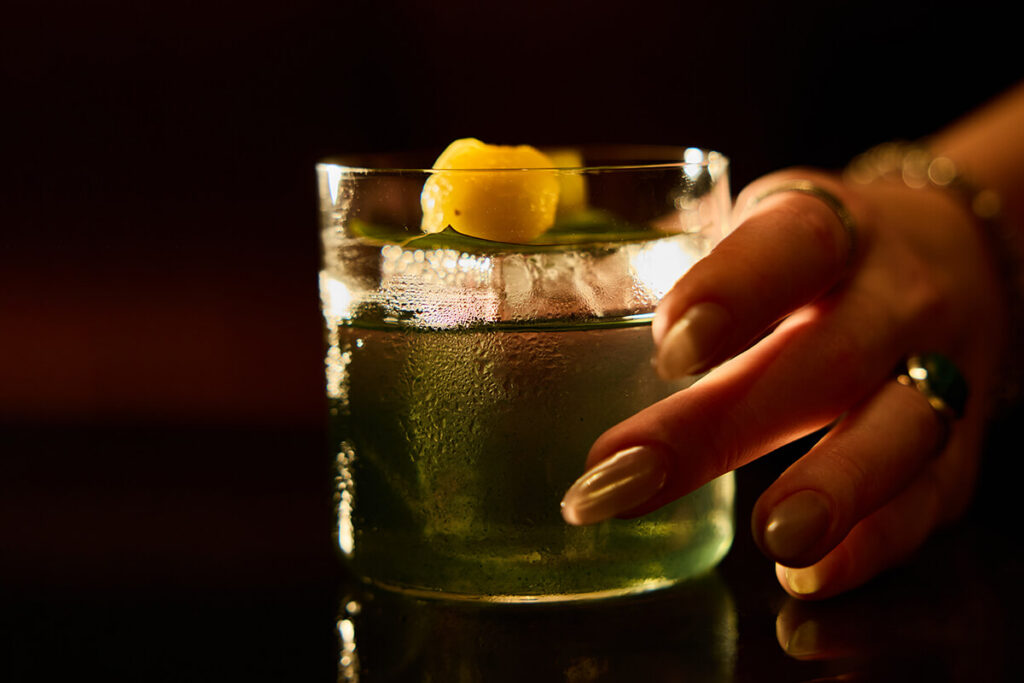 A vibrant, tropical Verdita cocktail served in a clear glass, showing its clarified milk punch texture with a subtle green tint from the mango tepache and tomatillo.